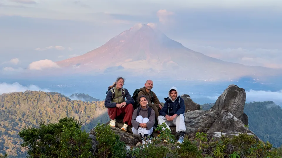 Guests resting at the Mount Sibayak summit with Mount Sinabung steaming behind