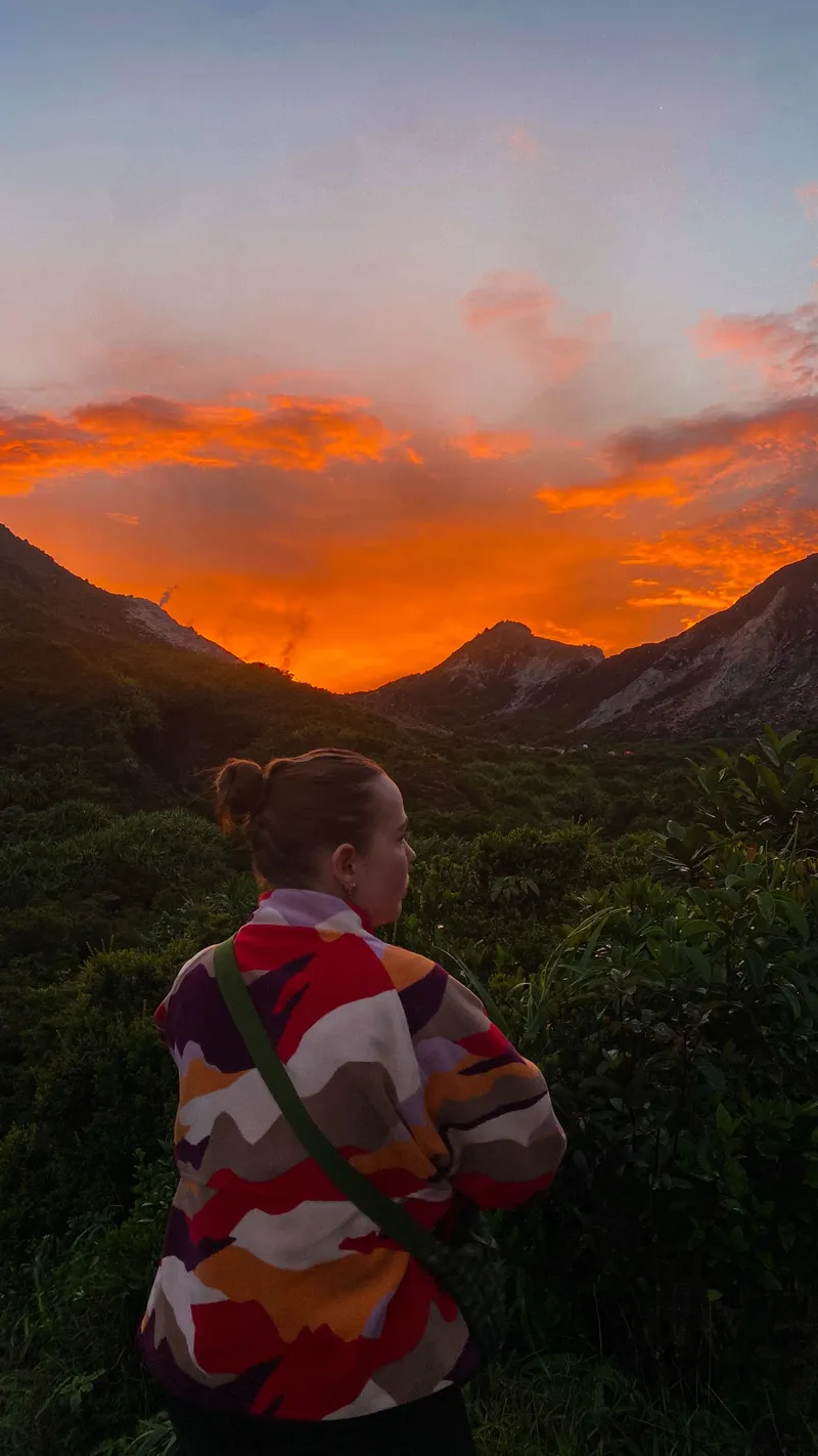 A trekker wrapped in a jacket watching the crater glow orange at sunrise