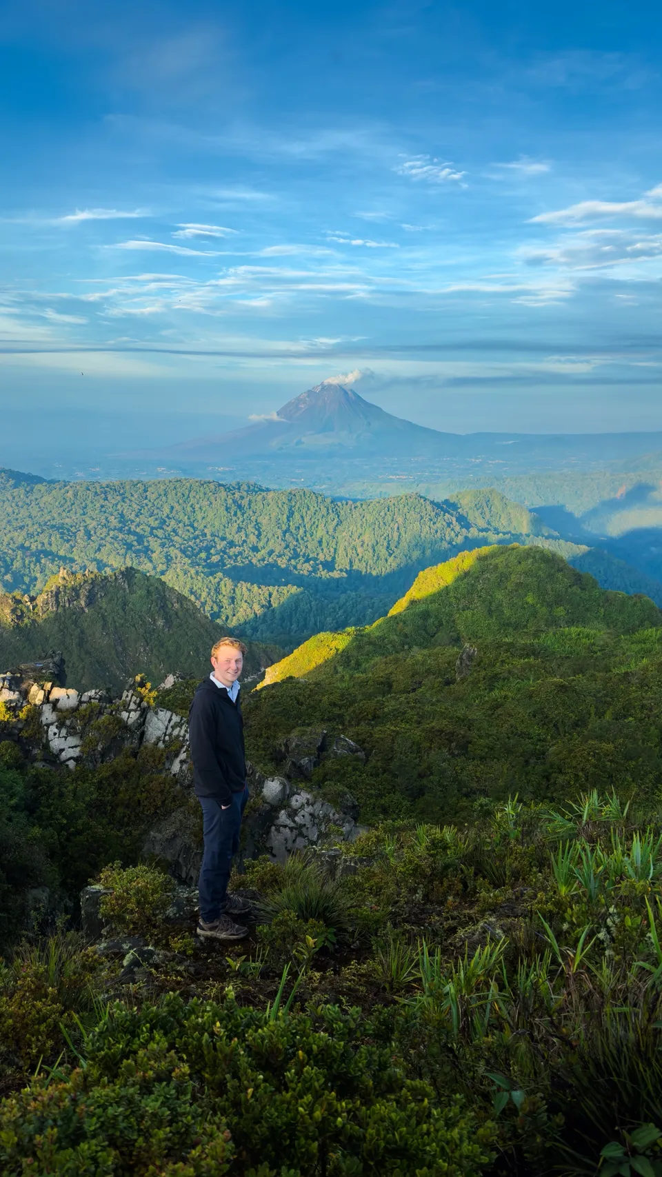 A hiker on the Mount Sibayak ridge with Mount Sinabung across the valley