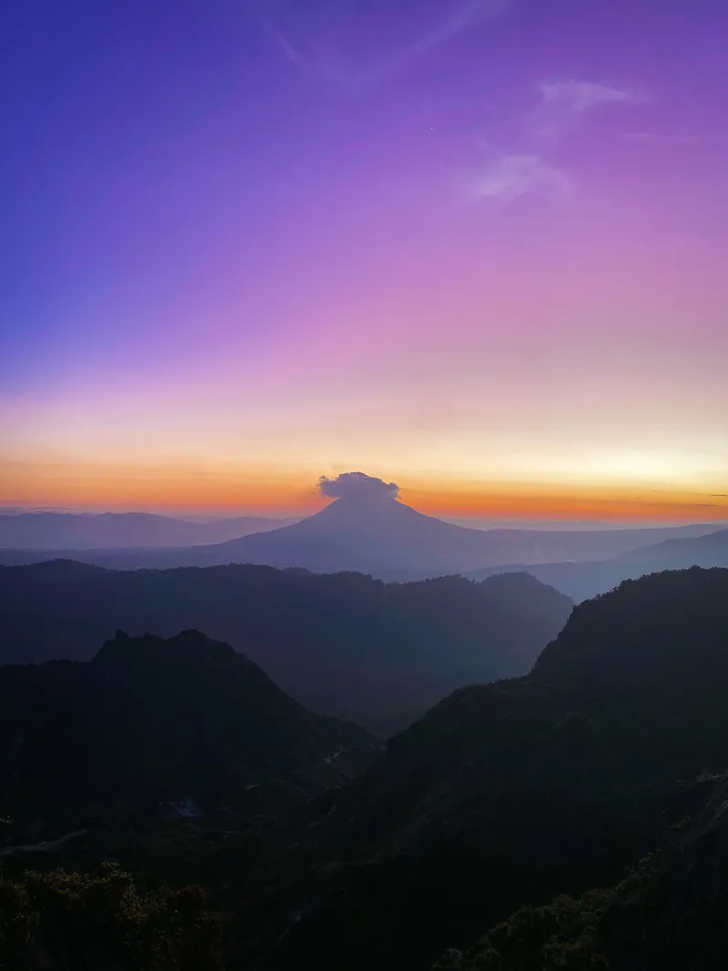 The purple and orange pre-dawn sky above the silhouette of Mount Sinabung